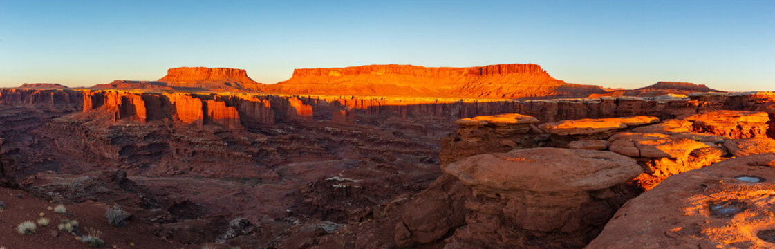 This scenic panorama of Canyonlands National Park features the sun's warm first light illuminating the Island in the Sky and reaching Monument Basin.