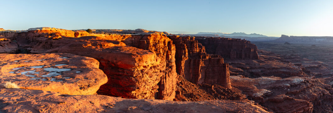 This scenic sunrise panorama of Canyonlands National Park near Moab, Utah, features warm light illuminating the canyon walls near Monument Basin.