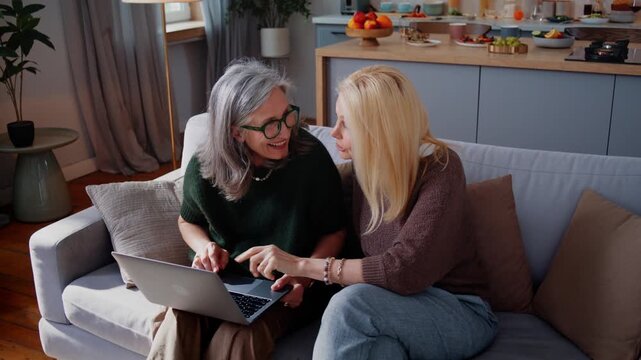 Senior women discuss laptop content with smiles sitting on sofa