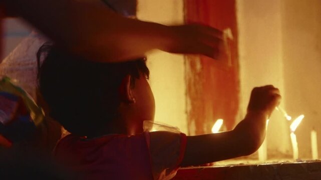 Young girl lighting a prayer candle during a religious ceremony inside an ancient asian temple
