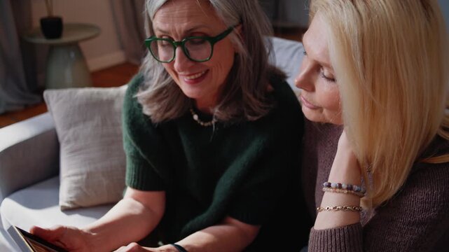 Senior women discuss framed photo while sitting close on sofa