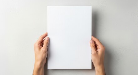 Fototapeta premium Hands hold a blank sheet of white paper against a neutral background.