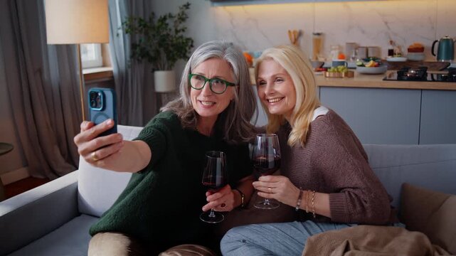 Senior women take selfie with wine glasses on sofa at home