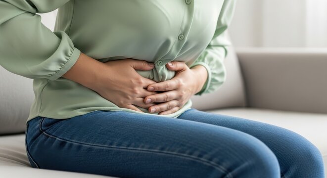 Woman experiences severe abdominal pain while sitting on a couch.