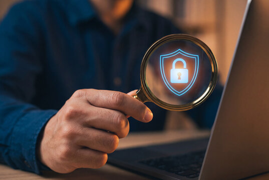 Hand with magnifying glass focusing on glowing digital lock and shield icon for security