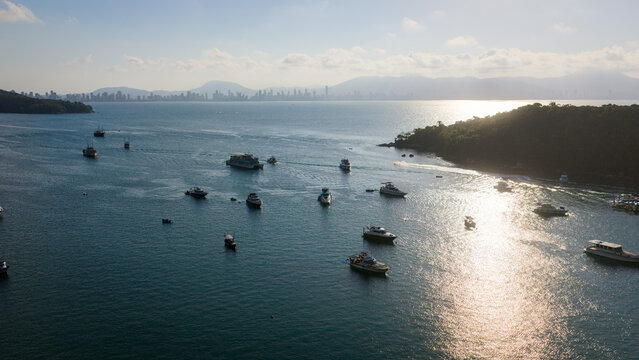 Boats scattered over calm ocean at sunset with golden reflection and distant coastline in Brazil.
