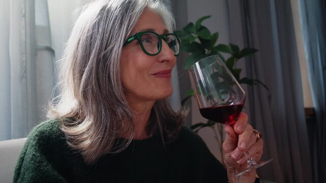 Elderly woman enjoys red wine with satisfied smile at home