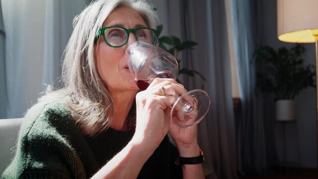 Senior woman savors red wine with calm smile at warm home