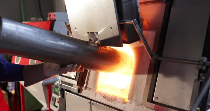Worker putting glass material into furnace in workshop, closeup