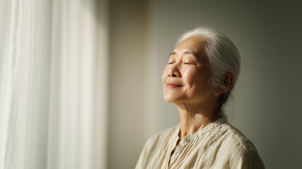 Fototapeta premium Radiant Senior Asian Woman with Silver Hair Smiling Peacefully in Sunlit Room