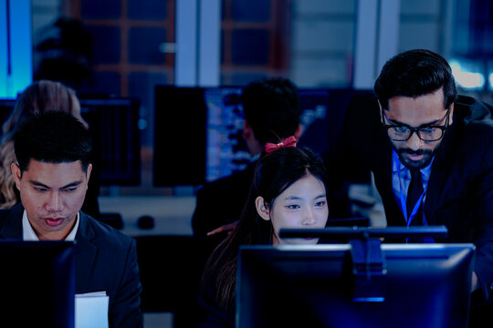 Diverse tech professionals collaborating intensely. Focused team synergy, reviewing project data side-by-side in a modern, blue-lit command center workspace.