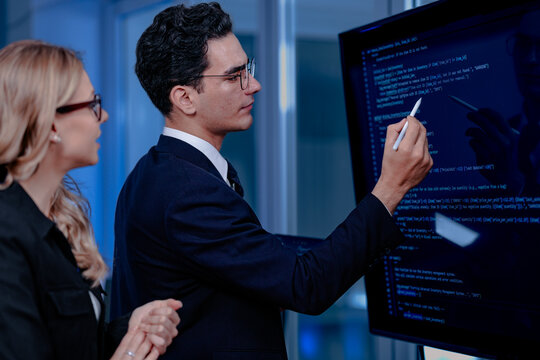 Code breakthrough achieved. Smiling senior developer points to a successful code segment on screen, sharing the solution with his colleague during a late night pair programming session.