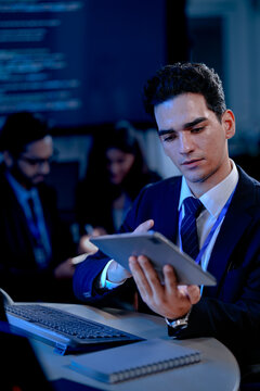 A data analyst scrolls through complex visualizations on a tablet comparing results against code displayed onscreen working late to finalize a critical business intelligence report.