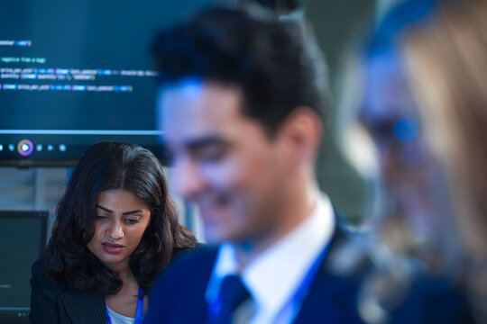 A focused young businessman in a suit interacts intently with his digital tablet late at night analyzing project data in a modern high tech office work environment.