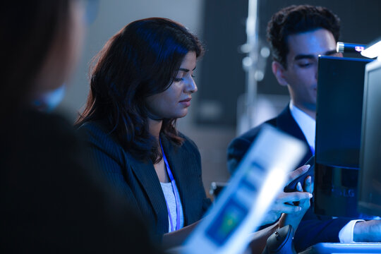 Monitoring AI training progress. Specialists oversee a machine learning model's training observing real time metrics on screen discussing adjustments via tablet interface late night.
