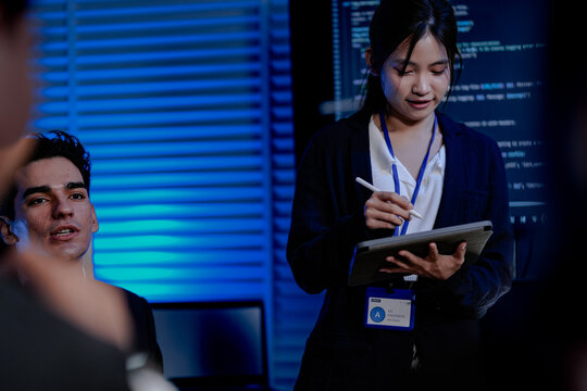 An Indian female developer leads a code review, holding a report. She explains a Python script for an AI or cybersecurity system to her team in a dark SOC Security Operations Center