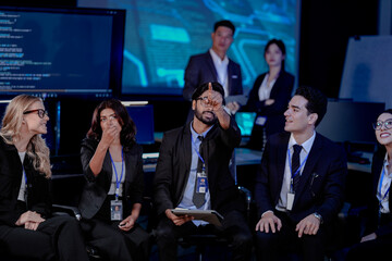 Obraz premium An Indian man with a tablet asks a question during a large team briefing. His diverse colleagues, including Indian and Caucasian women and men, listen in a high-tech conference room.