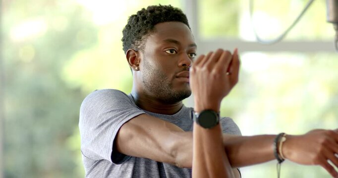 African American man warming up in gym grey tee pulling right arm across chest with smartwatch