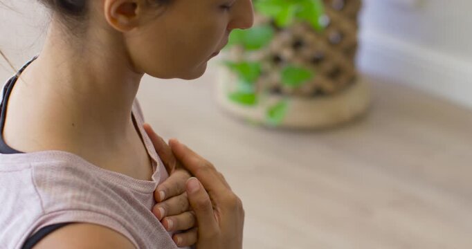 Woman placing both hands on upper chest, lowering chin and practicing breathwork in wellness space