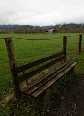 Fototapeta premium Wooden bench by wire fence in rural meadow with misty mountain view
