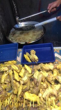 Street food vendor frying plantains and other savory snacks in a large wok at an outdoor market stall.