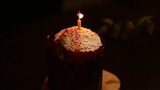 Easter cake with burning Easter candle on dark black background on natural wooden holder on a table. Close Up Easter holiday. No people