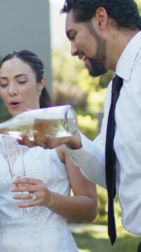 Vertical video: Pouring groom tipping bottle, filling bride's flute in garden, white lace wedding
