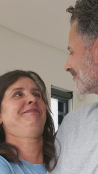 Vertical video: Smiling couple gazing, laughing, leaning at home, showing joy in blue by window