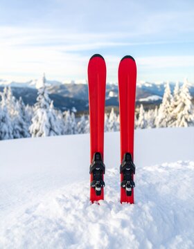 Bright red skis standing upright in fresh snow with snowy trees distant mountains and blue white winter sky