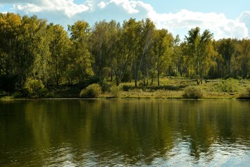 Obraz premium A ripple on the surface of a wide lake and the reflection of trees along its shores on a sunny summer day.