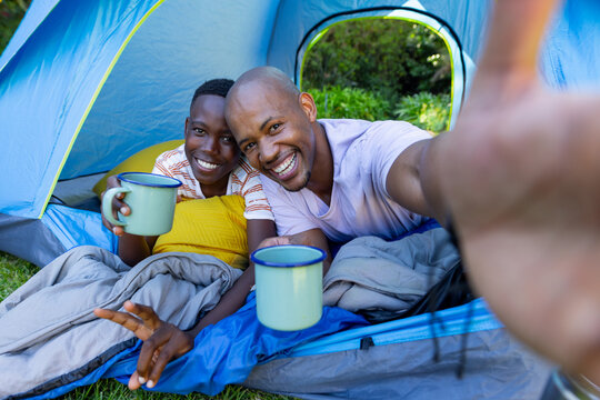 Vertical video: African American dad and son in blue tent with mugs, dad taking selfie to remember