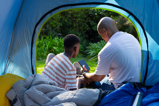 Receiving notification, African American father and adolescent son checking smartphone at blue tent