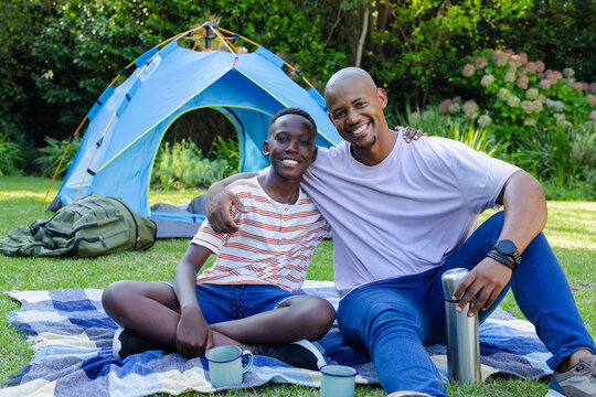 Vertical video: Dad and teen son sitting on blanket by tent sun warming holding thermos bonding