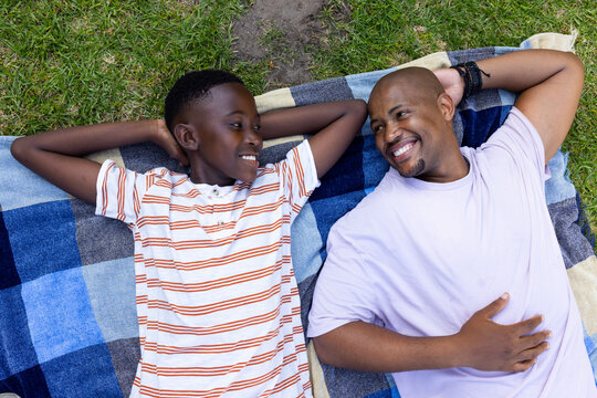 African American father and youth son reclining on checkered blanket in park, showing bracelets
