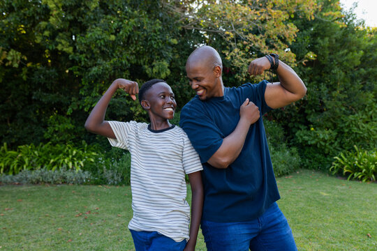 Father and youth son flexing biceps after smiling in backyard, showing playful bond with bracelets