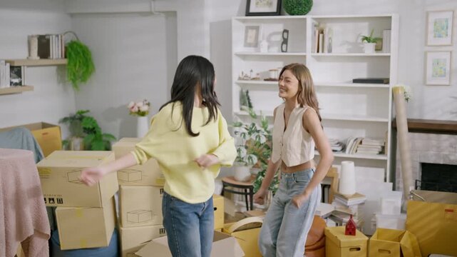 Moving apartment relocation with cardboard box unpacking new home living room young adult woman and friendship, joyful home interior as two women hug, laugh, and settle into their apartment together