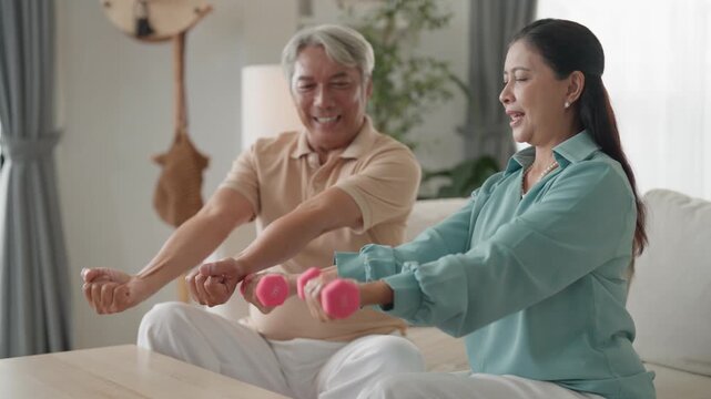 Senior couple high five living room happiness laughing home workout with dumbbell strength training, senior man and senior woman on sofa smile in bright living room, joyful bond and healthy lifestyle