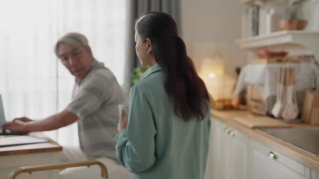 Senior man and adult woman at kitchen table with laptop in home office for online meeting and financial planning, couple family teamwork with caregiver support in warm remote work morning conversation