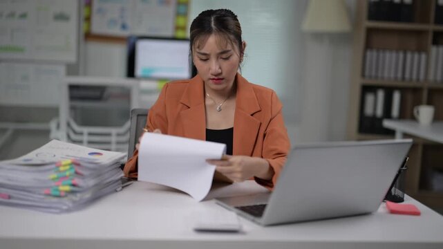 Young Woman Working at Desk with Laptop and Clipboard in Office