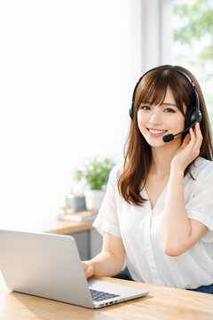 Smiling female customer support operator with headset using laptop at home office,ヘッドセットで対応する笑顔の女性オペレーターとノートパソコン、在宅ワークのイメージ