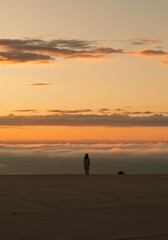 Fototapeta premium Lone woman standing on sand dunes watching the sunset over a layer of thick mist with orange clouds and copy space for a cinematic travel background