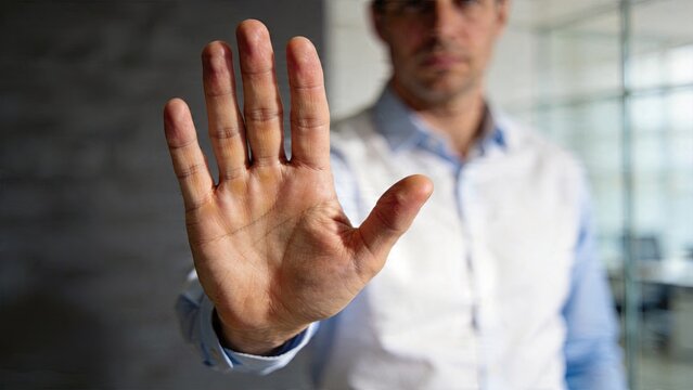 Businessman showing stop hand gesture in officeman refusing proposal with palm upcorporate rejection conceptprofessional saying no to dealauthority figure halting progress now