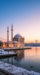 Fototapeta premium Historic mosque on the water edge featuring minarets and stone masonry with a suspension bridge stretching across the snowy winter horizon for travel editorial