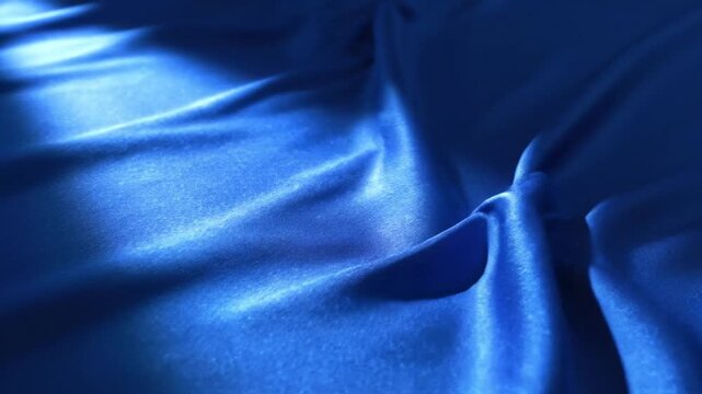 Abstract background featuring shiny blue fabric with prominent diagonal folds and sharp light reflections creating high contrast shadows on a shimmering textile surface texture.