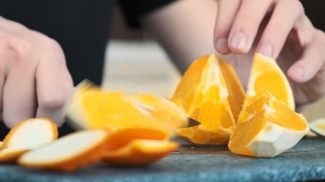 Chef cutting an orange in wedges on black cutting board close up slow motion footage.
