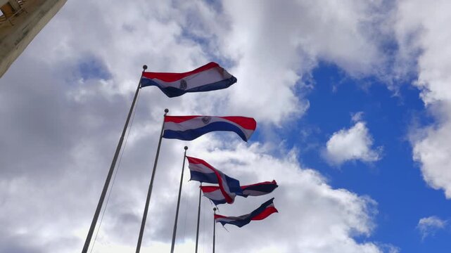 Waving Flags Against Cloudy Blue Sky In Plaza de Armas In Encarnaci&oacute;n, Paraguay. Low Angle Shot