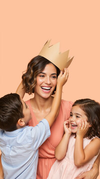 Vertical portrait of a happy mother being crowned by her children. Smiling woman with son and daughter on peach background. Queen for a day Mother's Day concept