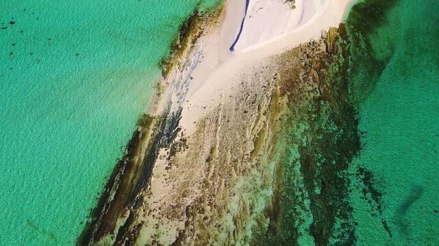 Cinematic drone view of a remote island paradise featuring a winding sandy peninsula and crystal-clear emerald sea.
