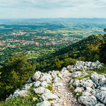 Rocky mountain path overlooking a picturesque town nestled in a vast green valley under a cloudy sky