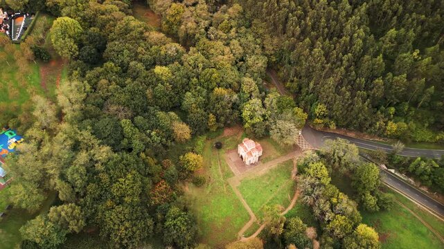 Isolated ancient stone church building on forest edge green mountain slopes aerial view.
